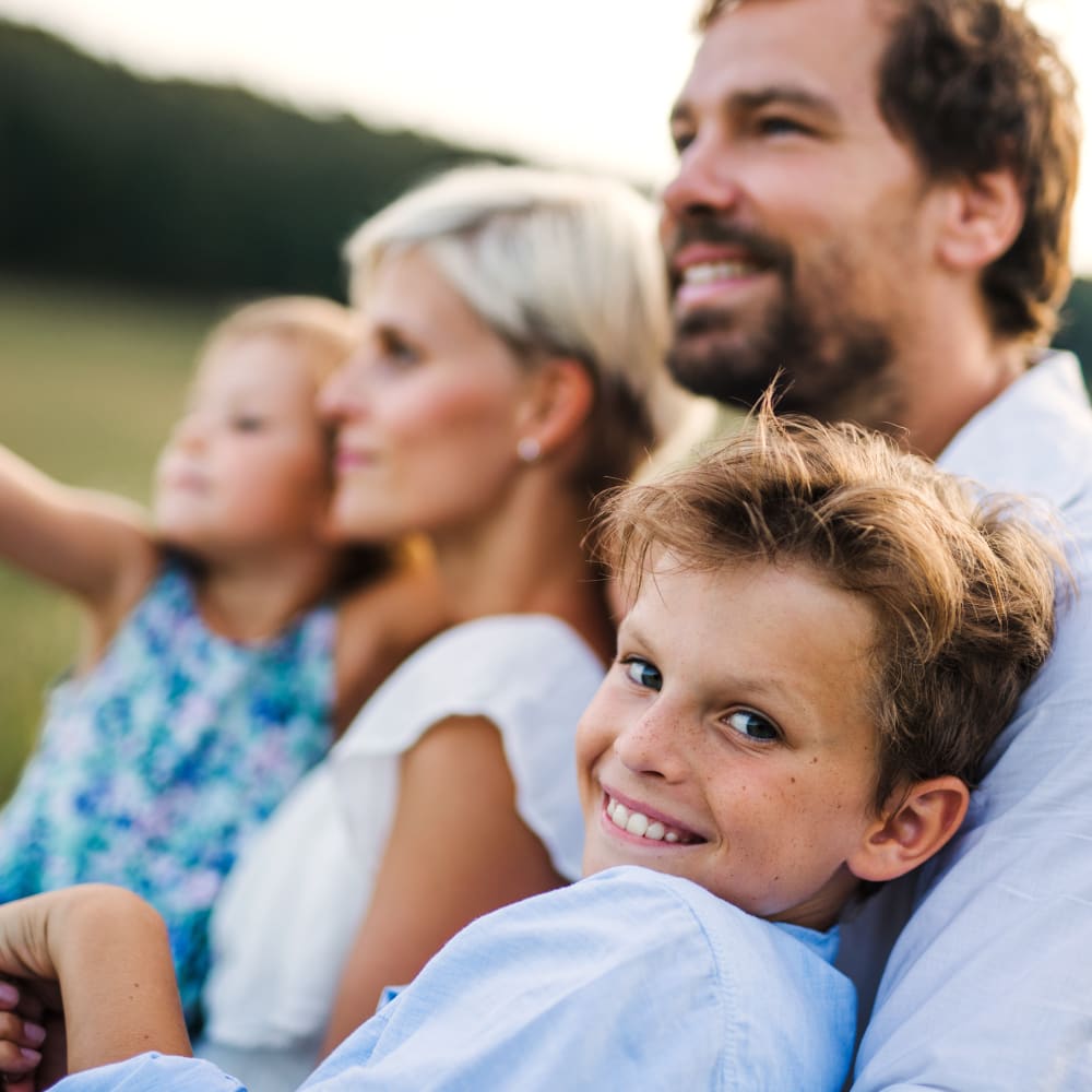 A family of four is sitting snuggled together outside. While three members of the family are looking forward, the young boy closest to the camera is looking over his shoulder at the camera.