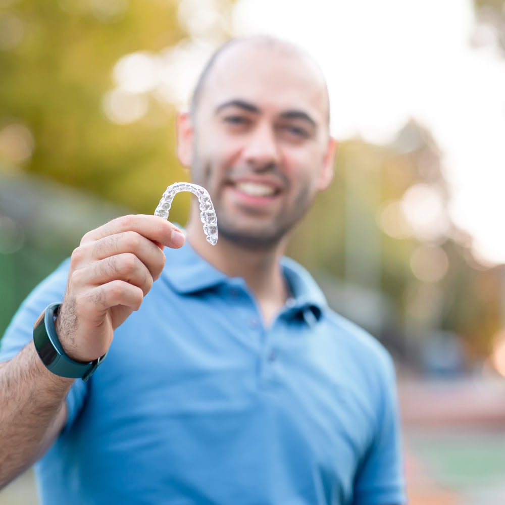 A man in a blue shirt is holding up an Invisalign clear aligner.