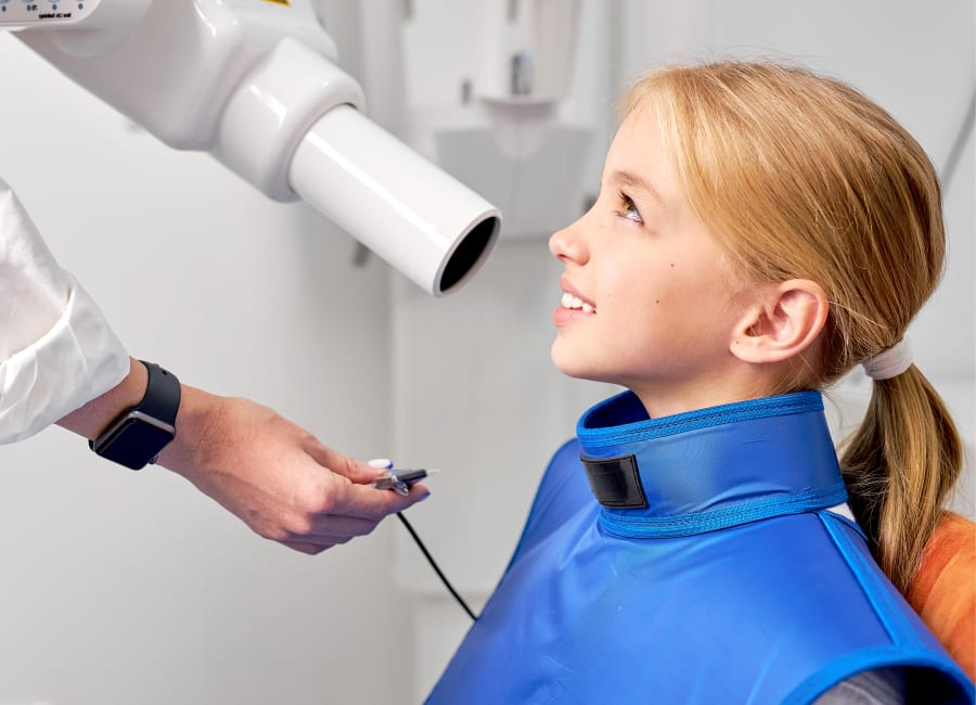 A dentist prepares a young girl for a dental X-ray.