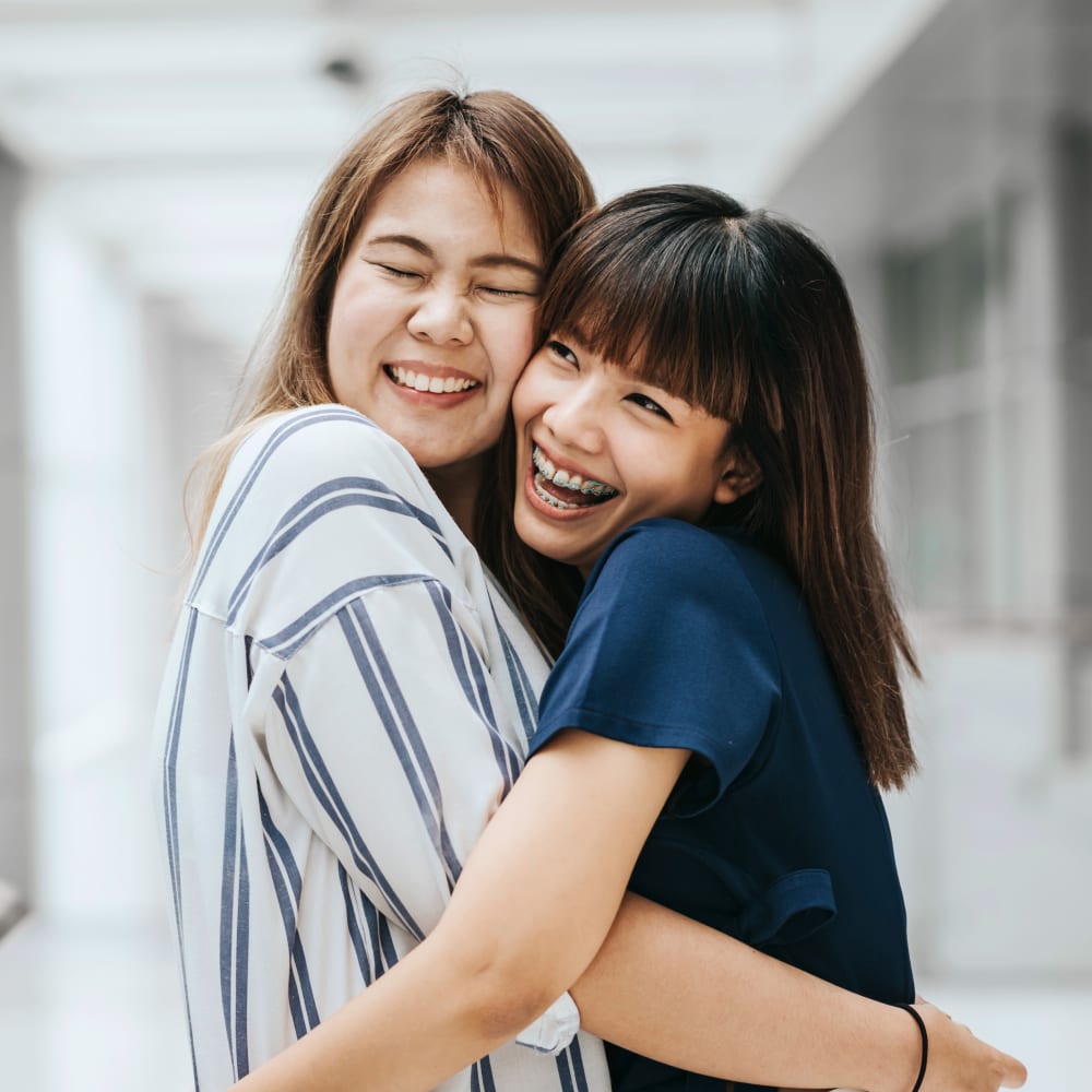Two teenage girls embrace enthusiastically. One of them has braces.